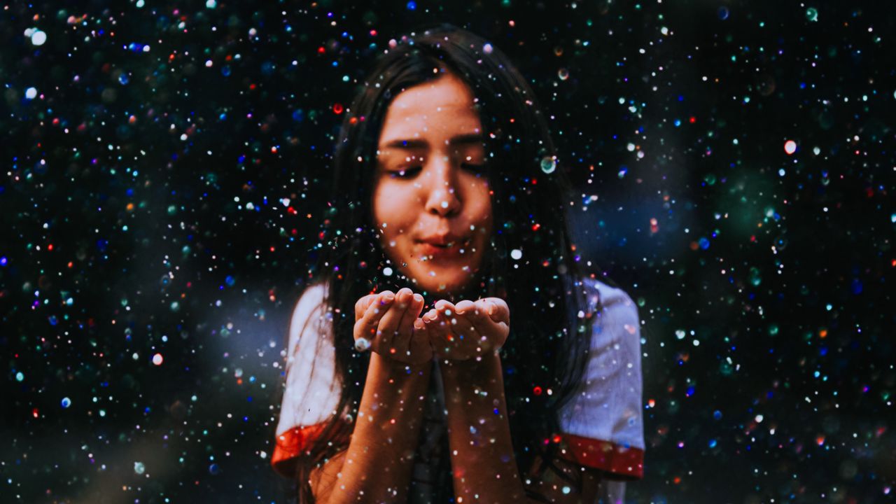 Joyful teenage girl blows vibrant particles, creating a magical atmosphere