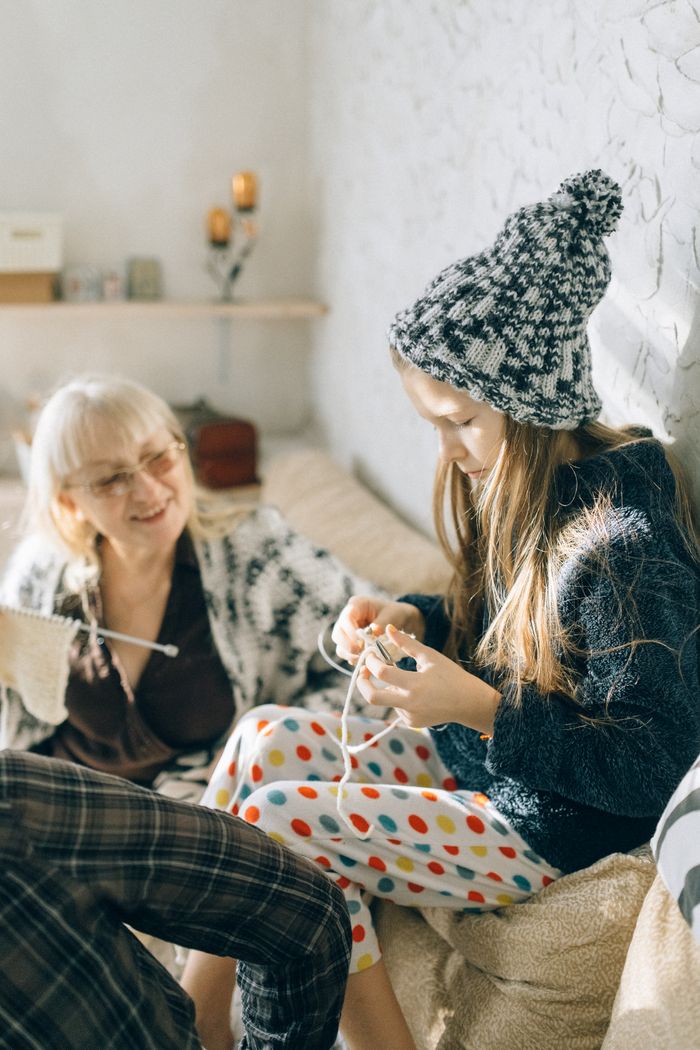 A loving moment of grandmother and granddaughter crocheting in a cozy room.
